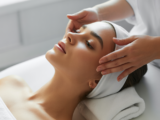 A professional spa facial treatment scene showing a relaxed woman receiving a customized facial from a skilled esthetician in a clean, bright setting.